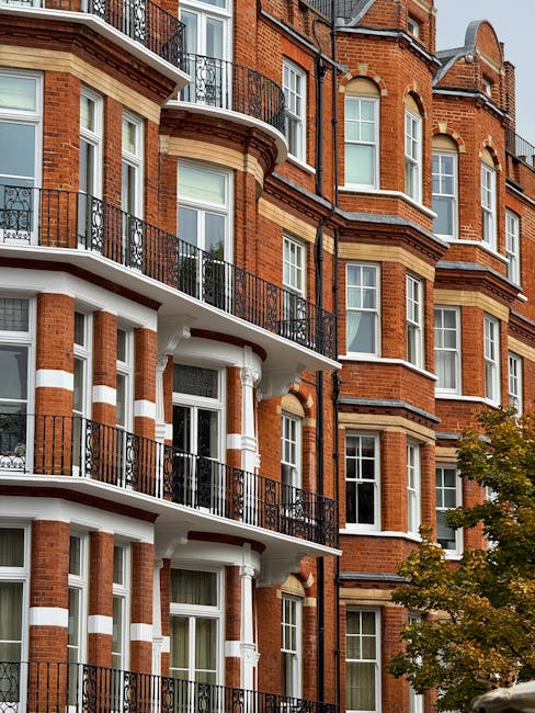 Exterior view of a multi-story residential building with red brick facade and white accents, showcasing curved balconies with black wrought iron railings, large windows, and decorative architectural d